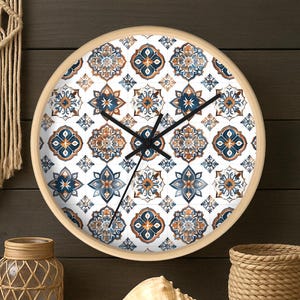 May include: Round wall clock with a light wood frame. The clock face features a repeating pattern of blue and orange floral tile designs on a white background. Black clock hands indicate the time.