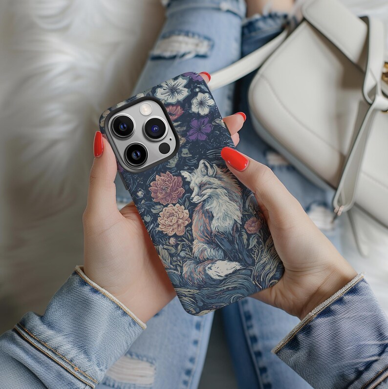 May include: A phone case featuring a detailed illustration of a fox amidst flowers. The case has a dark blue background with a floral pattern in shades of purple, pink, and white. The fox is depicted in shades of white, brown, and orange.