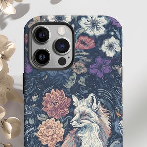 May include: A phone case featuring a detailed illustration of a fox with a floral background. The case has a dark blue base with flowers in shades of pink, purple, and white. The fox is depicted in shades of orange, white, and brown.