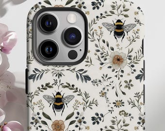 May include: A white phone case featuring a repeating pattern of bees, flowers, and foliage. The design includes detailed illustrations of bumblebees with black and yellow stripes, along with various floral elements in shades of white, brown, and green.
