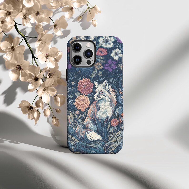 May include: A phone case featuring a detailed illustration of a fox amidst a floral garden. The case has a dark blue background with pink, purple, and white flowers. The fox is depicted with orange and white fur, adding a touch of nature-inspired art.