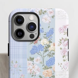 May include: A blue and white floral phone case with a checkered pattern and a white lace design. The case has a cutout for the camera lens.