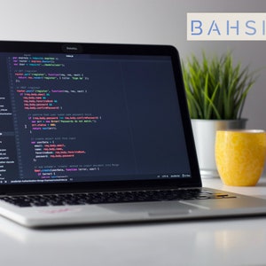 May include: A silver laptop computer with a dark screen displaying code in multiple colors. The laptop is on a white table with a potted plant and a yellow glass on the right side of the screen. The text "BAHSIC" is visible in the upper right corner of the image.