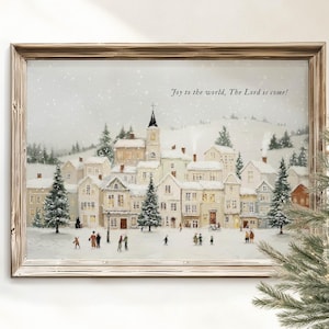 Puede incluir: Una escena invernal enmarcada representa un pueblo nevado con edificios, una iglesia y personas. La obra de arte está enmarcada en un marco de madera marrón claro. El texto "Joy to the world, The Lord is come!" está escrito en la parte superior.