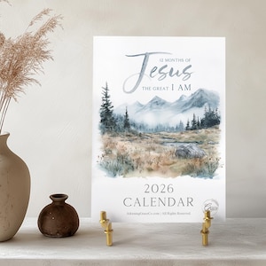May include: A 2026 calendar featuring a watercolor landscape with mountains and trees. The text "12 Months of Jesus, The Great I AM" is at the top. The calendar is displayed on a white surface with a vase of dried plants and a small brown vase.