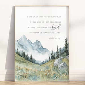 May include: Framed watercolour print depicting a mountain landscape with text from Psalms 121:1-2. The artwork shows a valley with mountains, trees, and wildflowers in green, blue, and beige. The text reads, "I lift up my eyes to the mountains..."