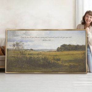 Puede incluir: Una impresión artística enmarcada de un paisaje con un marco dorado. La obra de arte representa una escena pastoral con campos, árboles y un cielo nublado. El texto en la parte superior dice: "Venid a mí, todos los que estáis cansados y agobiados, y yo os daré descanso."