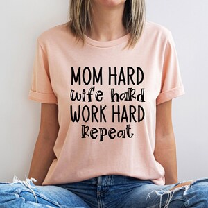 May include: A peach-colored t-shirt with the text "MOM HARD wife hard WORK HARD repeat" printed in black.