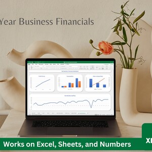 May include: A laptop computer displaying a spreadsheet with charts and graphs. The spreadsheet is titled "My Business Financials Dashboard". The laptop is on a white table with a vase of flowers and decorative ceramic sculptures. The text "3-Year Business Financials" is at the top of the image. The text "Works on Excel, Sheets, and Numbers" is at the bottom of the image. The file extension "XLS" is in the lower right corner of the image.