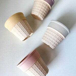 May include: Four ceramic ice cream cone-shaped planters in pastel colors. Each planter has a waffle cone texture on the bottom and a solid color rim. Colors include yellow, pink, purple, and gray. These planters are ideal for small succulents or herbs.