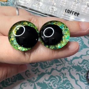 May include: Two green and black glitter doll eyes with a white ring around the black pupil.
