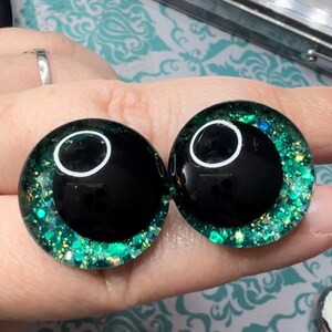 May include: Two black and green glitter doll eyes with a white pupil.