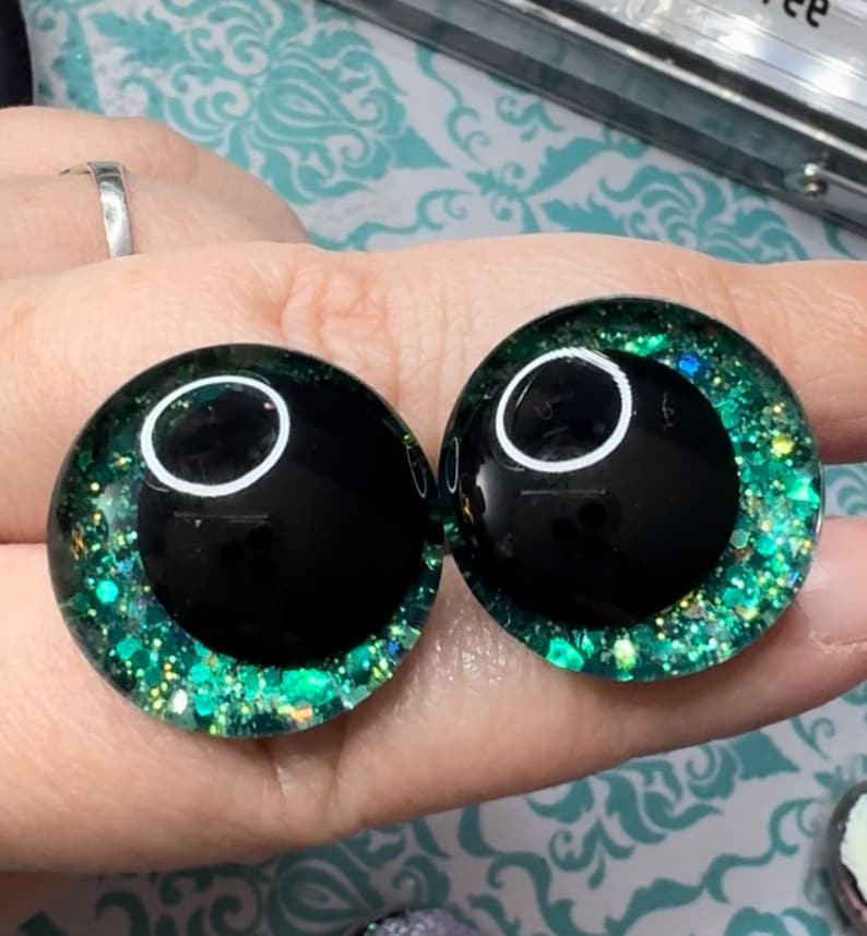 May include: Two black and green glitter doll eyes with a white pupil.