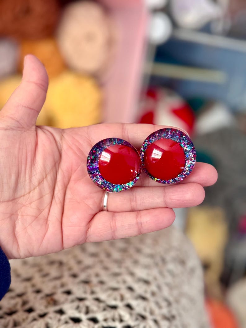 May include: Two red round resin buttons with a glittery purple, blue, and green border.