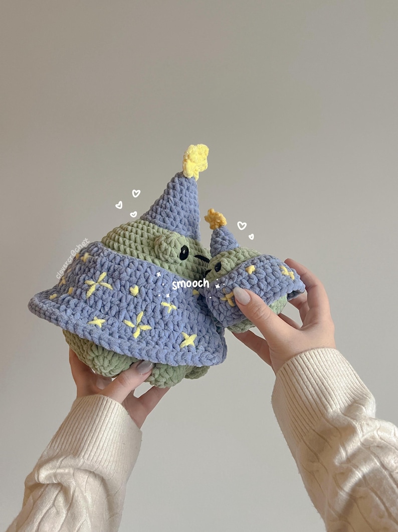May include: Two crocheted plush toys shaped like a creature wearing a party hat. The larger toy is green and blue with yellow stars. The smaller toy is green with a yellow star on its hat. The text "smooch" is written on the larger toy.