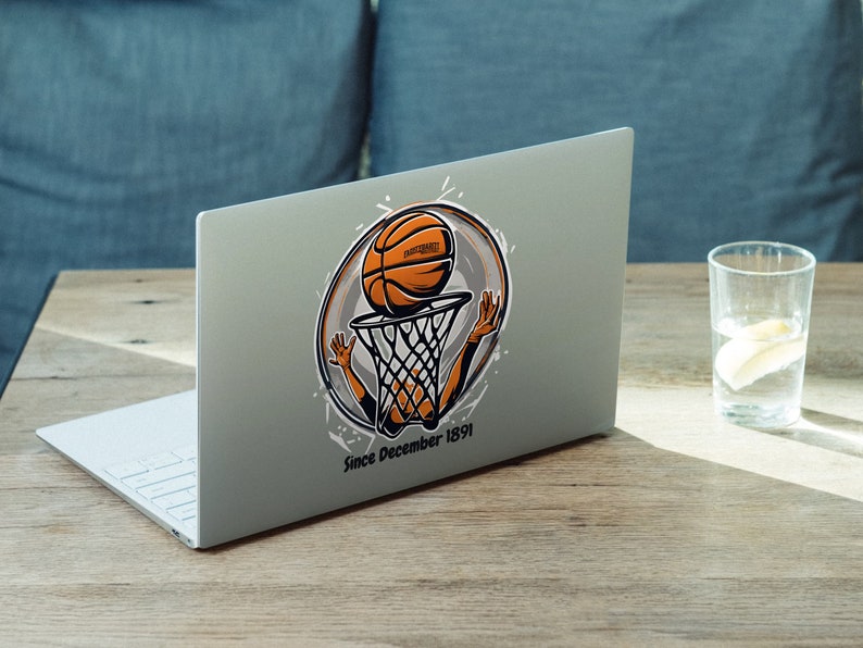 以下が含まれることがあります： バスケットボールの漫画のキャラクターがバスケットボールをゴールにダンクシュートしているステッカーが貼られたシルバーのラップトップ。ステッカーには「Since December 1891」という文字が書かれている。