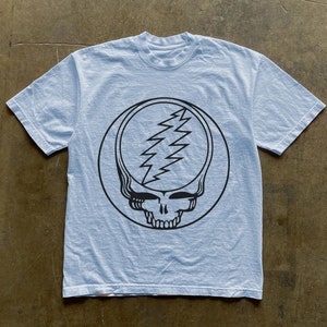 May include: A light blue t-shirt with a black and white graphic of the Grateful Dead's iconic Steal Your Face logo.