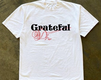 May include: White t-shirt with a black graphic of a rose and the word "Grateful" in black.