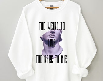 May include: White sweatshirt with a graphic print of a broken statue and the text "Too Weird To Live Too Rare To Die."