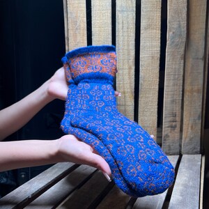 May include: A pair of blue and orange patterned socks. The socks are held up, showcasing the detailed knit design. The cuff and the body of the socks feature a contrasting color pattern.