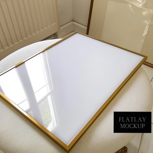 May include: A gold-colored picture frame with a white background. The frame is lying on a white surface with the text "FLATLAY MOCKUP" in black.