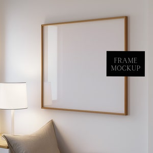 Pode incluir: Uma maquete de moldura dourada pendurada em uma parede branca. A moldura está vazia e pronta para sua obra de arte ou foto. O texto "FRAME MOCKUP" está impresso em preto em um retângulo preto.