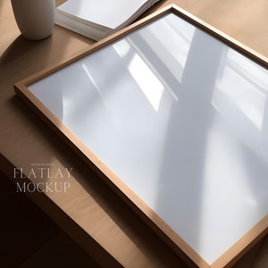 May include: A wooden picture frame with a white mat and a white background. The frame is sitting on a light brown wooden surface. The text "FLATLAY MOCKUP" is visible in the lower left corner of the image.