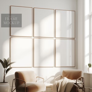 Op de afbeelding: Een witte muur met zes lege fotolijsten in een rasterpatroon. De lijsten zijn gemaakt van dun, goudkleurig metaal. Twee bruine fauteuils met dekens staan voor de lijsten. Een kleine plant in een pot staat aan de linkerkant van de afbeelding.