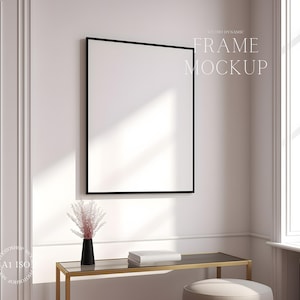 Pu&ograve; includere: Un mockup di cornice nera appeso a una parete bianca con un tavolo dorato e un vaso con fiori rosa di fronte.