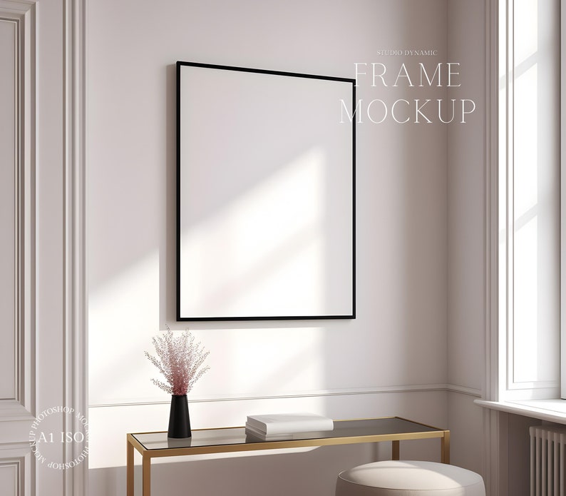 Pu&ograve; includere: Un mockup di cornice nera appeso a una parete bianca con un tavolo dorato e un vaso con fiori rosa di fronte.