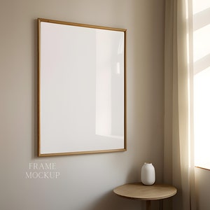Könnte beinhalten: Ein Holzrahmen-Mockup mit weißem Hintergrund, der an einer hellbeigen Wand hängt. Eine kleine weiße Vase steht auf einem Holztisch in der Ecke des Raumes.