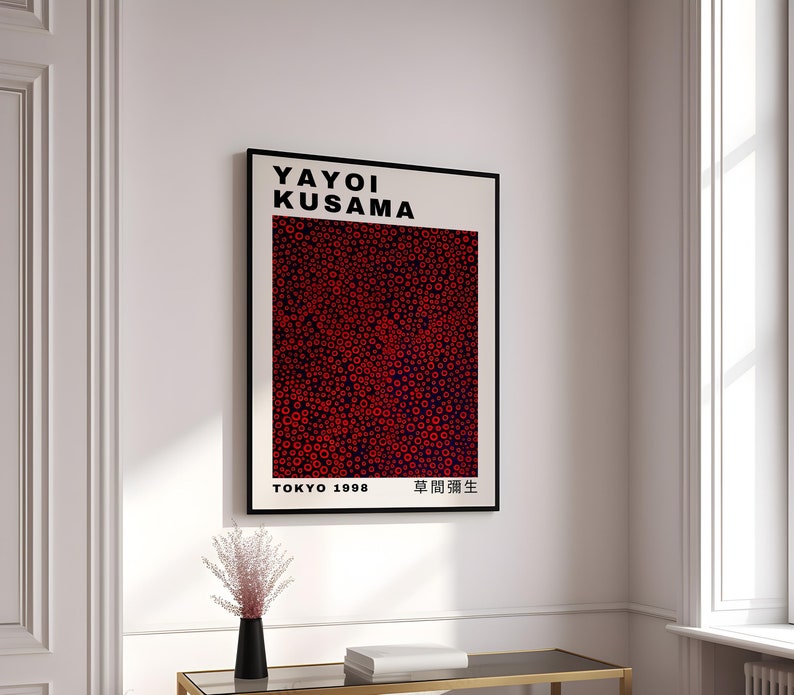 Pu&ograve; includere: Un poster in bianco e nero con il testo "Yayoi Kusama" in grassetto, lettere nere. Il poster presenta un motivo astratto rosso e nero di cerchi e il testo "Tokyo 1998" e "草間彌生" in lettere nere.