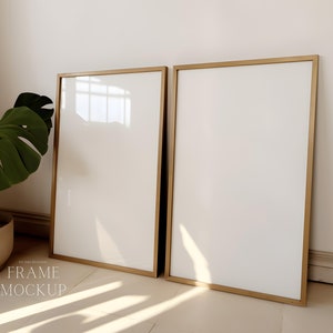 Könnte beinhalten: Zwei goldfarbene Bilderrahmen mit weißen Passepartouts lehnen an einer weißen Wand. Die Rahmen sind leer und bereit für ein Foto oder ein Kunstwerk.