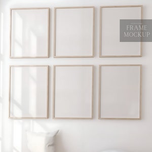 Op de afbeelding: Zes lege fotolijsten met lichte houten frames zijn in een rasterpatroon op een witte muur gerangschikt. De frames zijn allemaal even groot en gelijkmatig verdeeld.