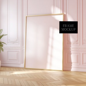 May include: A gold frame mockup in a pink room with white trim and a plant in a white pot. The frame is empty and ready for your design.