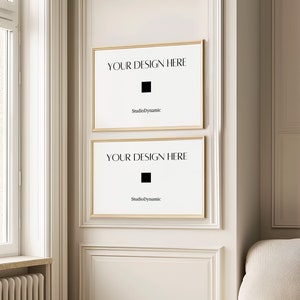 May include: Two gold framed posters with white backgrounds and black text that reads "YOUR DESIGN HERE" and "StudioDynamic". The posters are hanging on a white wall with gold trim.