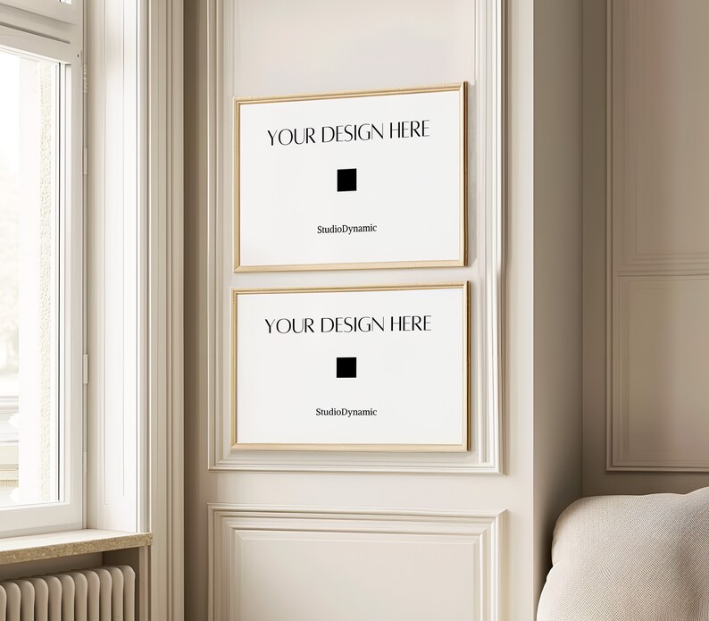 May include: Two gold framed posters with white backgrounds and black text that reads "YOUR DESIGN HERE" and "StudioDynamic". The posters are hanging on a white wall with gold trim.