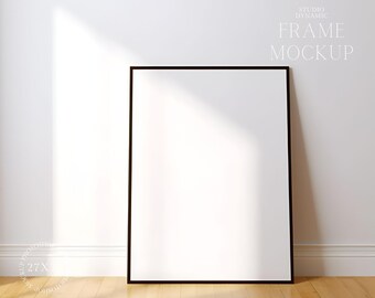 Könnte beinhalten: Ein schwarzer Rahmen-Mockup mit weißem Hintergrund. Der Rahmen steht auf einem Holzboden mit einer weißen Wand dahinter. Der Text "STUDIO DYNAMIC FRAME MOCKUP" befindet sich in der oberen rechten Ecke des Bildes.