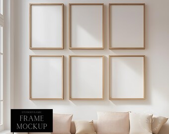 Op de afbeelding: Zes lege fotolijsten met een lichte houten afwerking zijn in een rasterpatroon op een witte muur gerangschikt. De lijsten zijn allemaal even groot en gelijkmatig geplaatst. Een witte bank met beige kussens bevindt zich op de voorgrond.
