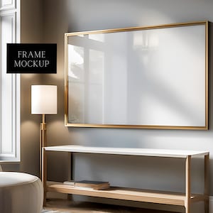 Può includere: Un mockup di cornice dorata appeso a una parete grigio chiaro sopra un tavolino da console bianco e legno. La cornice è vuota e pronta per il tuo design.