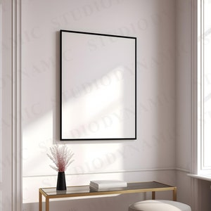 Pu&ograve; includere: Un quadro incorniciato nero appeso a una parete bianca sopra un tavolo in metallo dorato con un vaso di fiori secchi rosa e una pila di libri.