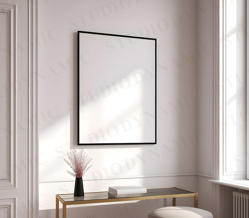 Pu&ograve; includere: Un quadro incorniciato nero appeso a una parete bianca sopra un tavolo in metallo dorato con un vaso di fiori secchi rosa e una pila di libri.