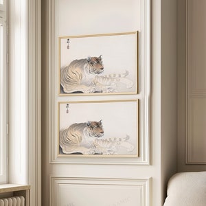 May include: Two framed prints of a tiger lying down. The tiger is brown and black with white stripes. The prints are in a gold frame and have a white background.