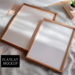 May include: Two wooden picture frames with white mats on a light gray and white patterned fabric background. The frames are empty and ready for your photos or artwork.  "FLATLAY MOCKUP" is written in black text on a black rectangle.