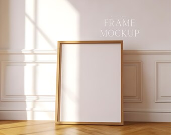 Può includere: Un mockup di una cornice in legno chiaro con sfondo bianco, in piedi su un pavimento in legno chiaro. La cornice è in una stanza con pareti bianche e modanature bianche.