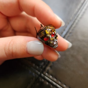 May include: A black metal skull charm with red rhinestone eyes.