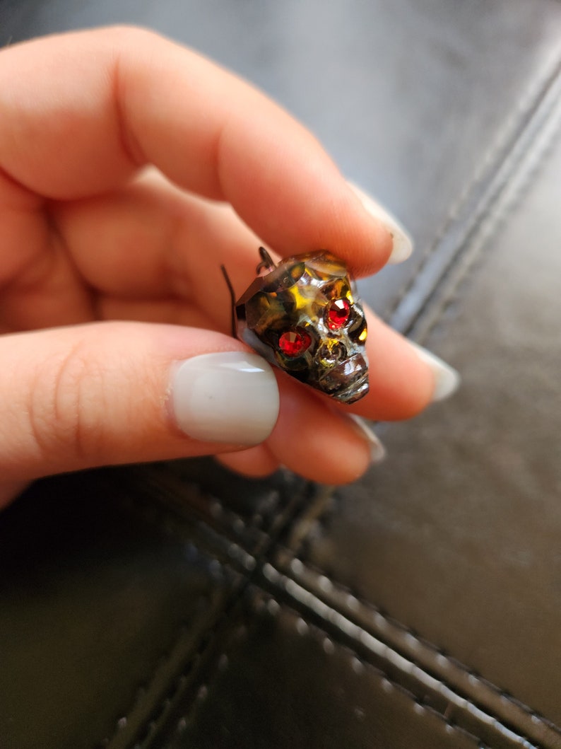May include: A black metal skull charm with red rhinestone eyes.