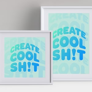 May include: Two framed art prints with white frames. The prints feature the phrase "CREATE COOL SH!T" in a gradient of blue and teal. The background has a faded version of the same text. The art is displayed on a light gray background.