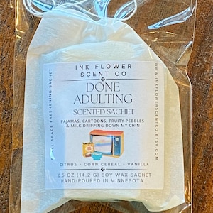 May include: A clear plastic bag containing a white scented sachet. The sachet has text that reads "DONE ADULTING" and "SCENTED SACHET". The sachet is labeled "INK FLOWER SCENT CO" and lists the scent as citrus, corn cereal, and vanilla. The sachet is 0.5 oz (14.2 g) and hand-poured in Minnesota.