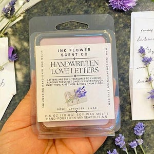 May include: A pink soy wax melt in a clear plastic container with the text "Ink Flower Scent Co. Handwritten Love Letters" and "Rose - Lavender - Lilac 2.5 oz (70.8g) Soy Wax Melts Hand-Poured in Minneapolis, MN".